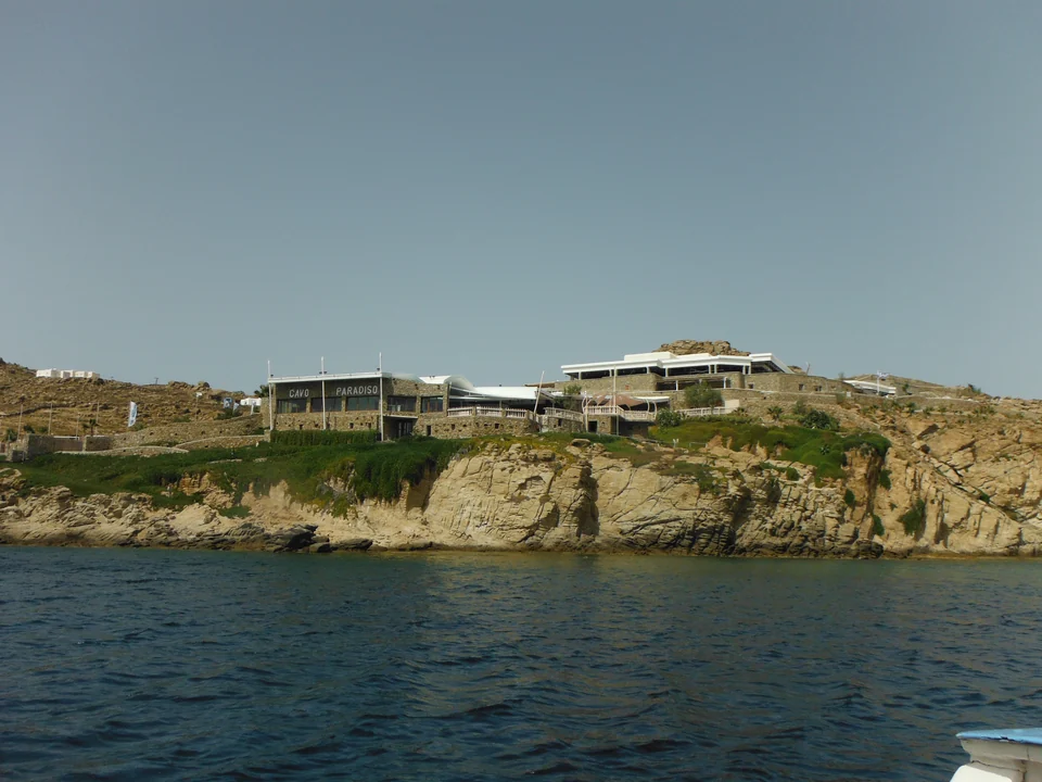 Πέτρινα κτίρια του Cavo Paradiso πάνω από βραχώδη ακτή, όπως φαίνονται από τη θάλασσα