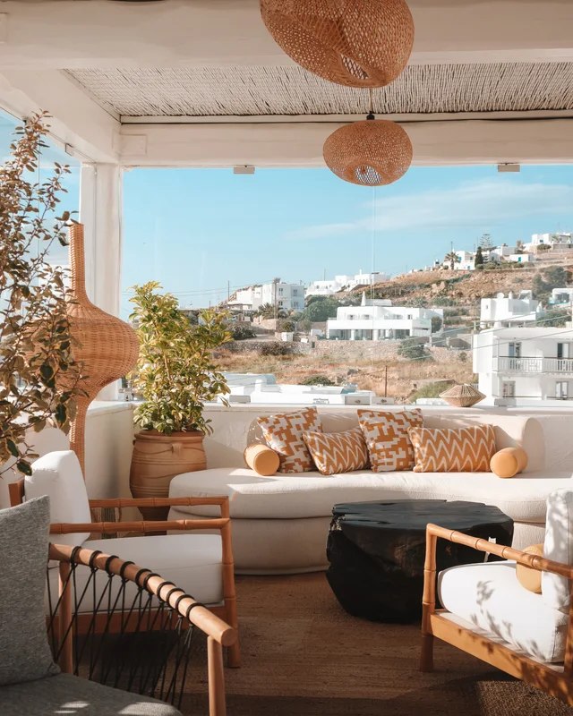Καθιστικό στην ταράτσα του Kove Hotel & Spa Mykonos, με πλεκτά κρεμαστά φωτιστικά και λευκά κυκλαδίτικα κτίρια στο βάθος
