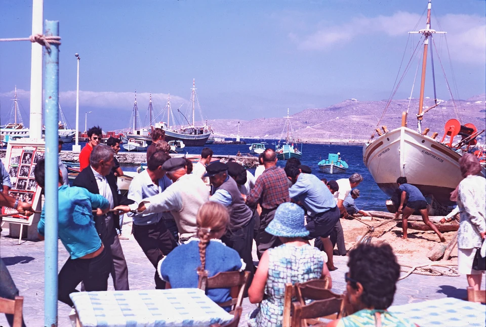 People haul a boat ashore beside waterfront café tables and moored vessels